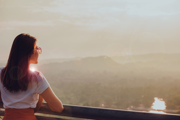 Woman standing on the mountain top looking at panoramic view of mountain range in the mist under the sunrise