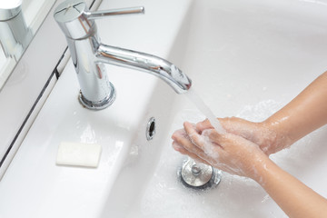 Kid washing hands in a white basin with a bar of white soap.