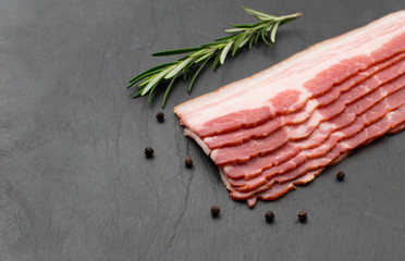Thinly sliced strips of bacon lie on a dark slate background