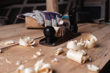 Old retro hand planer with gloves and mallet on wooden table with sawdust and shavings. carpentry, wood roofing, wood workshop
