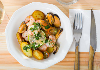 Tasty warm salad with fried potatoes, shrimp and mussels, served at plate