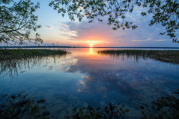 Fototapeta premium The rays of the dawn sun on the lake. Reflection of sunset clouds in the river. Rural landscape.