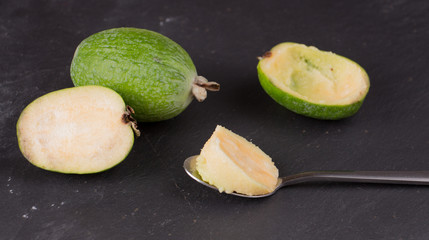 Cut fruit of the mature feijoa on a dark slate background. Pulp fruit on the bark spoon