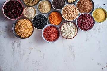 Organic superfood assortment in bowls. With raw peas, beans, wild rice, lentil, Goji berries, cranberry, couscous, linseeds on white rusty background. Above view.