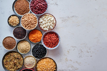 Organic superfood assortment in bowls. With raw peas, beans, wild rice, lentil, Goji berries, cranberry, couscous, linseeds on white rusty background. Above view.