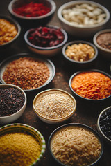 Various superfoods in smal bowls on dark rusty background. Superfood as rice, lentil, beans, peas, goji, flaxseed, buckwheat, couscous, chickpeas Above view Flat lay