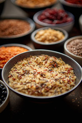 Raw wild rice in ceramic bowl. Composition of superfoods in background. Placed on dark rusty table. Selective focus.