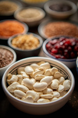 Raw white bean in ceramic bowl. Composition of superfoods in background. Placed on dark rusty table. Selective focus.