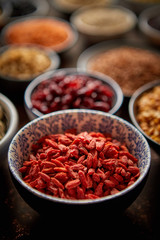 Raw goji berries in ceramic bowl. Composition of superfoods in background. Placed on dark rusty table. Selective focus.