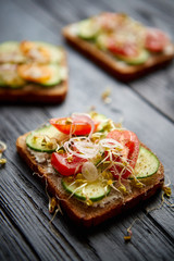 Healthy vege toasts with onion, cucomber, cherry tomatoes, crumbled feta cheese and radish sprouts. Table top view on black wooden background