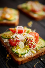 Healthy vege toasts with onion, cucomber, cherry tomatoes, crumbled feta cheese and radish sprouts. Table top view on black wooden background