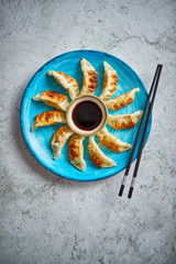 Traditional asian dumplings Gyozas on turqoise ceramic hand painted plate served with chopsticks and bowl of soy sauce over concrete texture background. Top view with copy space.