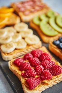 Six Healthy breakfast toasts. Wholegrain bread slices with peanut butter and various fruits. Served on grey cutting board. Top view, grey stone background. Dieting concept with cpoy space