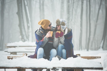 Young couple with blanket drinking coffee outdoors in snow