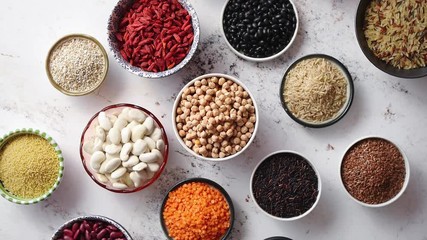 Organic superfood assortment in bowls. With raw peas, beans, wild rice, lentil, Goji berries, cranberry, couscous, linseeds on white rusty background. Above view.