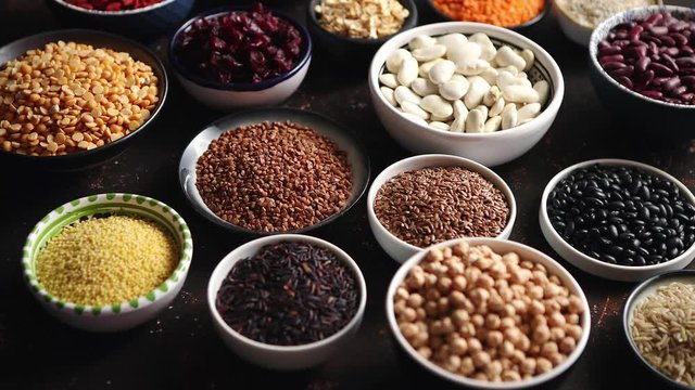 Various superfoods in smal bowls on dark rusty background. Superfood as rice, lentil, beans, peas, goji, flaxseed, buckwheat, couscous, chickpeas Above view Flat lay