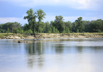 Cloudy and beautiful day on the river Desna in Ukraine, sun breaking through clouds highlights the water, trees and steep bank are reflected in the water, it seems it is going to rain