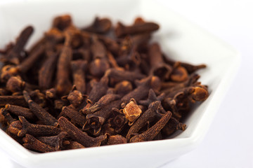Spice cloves in a small white ceramic dish isolated on white background