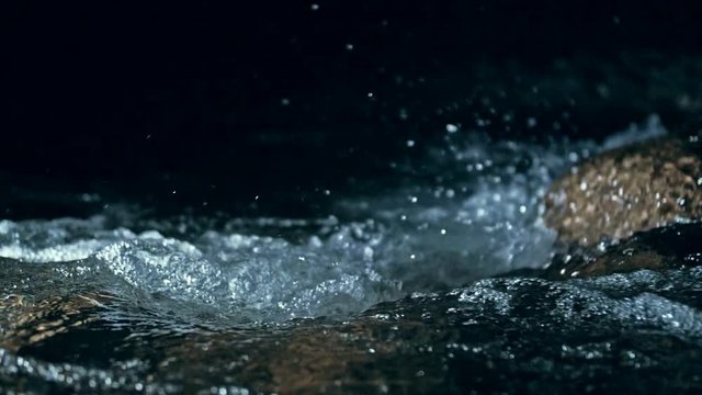 Slow motion of waves on dark water surface with play of flecks of bright light close up. Amazing dramatic natural background. Shooting with 180fps. Epic mystical and magic night view. Crystal clear
