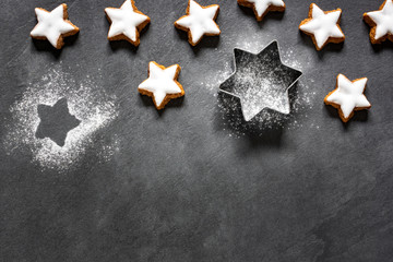 Fresh cinnamon star shaped cookies with frosting on black slate background