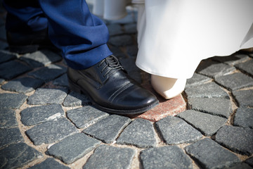 Feet in the shoes of the bride and Groom on the pavement. Beautiful Wedding ceremony in moments.