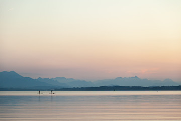 A couple practicing paddlesurf at sunset on a lake