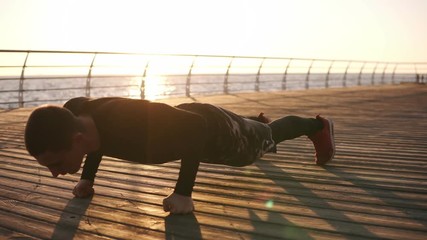 Young athlete doing push ups on his fists outdoors on the wooden froor in front the sea or ocean. Fitness and exercising on the seaside. Sport, recreation, boxing lifestyle concept