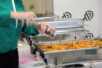 Catering, jedzenie, kelnerka przyprawia jedzenie na stalowej patelni na szwedzkim stole.