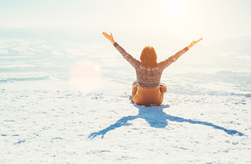 Happy woman sits on the snowy mountain hill over the city. Sunny winter day