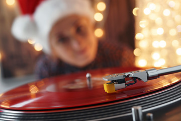 Blurred Image of Christmas. Turntable vinyl record player. Sound technology for DJ to mix & play music. Blurred a girl in a Christmas cap with red hair listening to a vinyl record in the background
