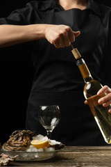 Obraz premium Chef opens Italian dry wine with oysters with lemon, on a dark background
