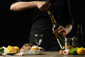 Chef opens Italian dry wine with oysters with lemon, on a dark background