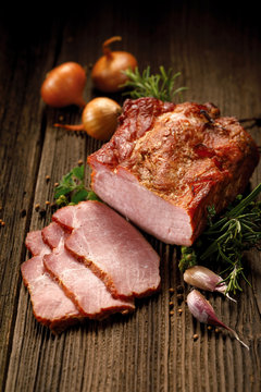 Smoked meats, sliced smoked pork loin on a wooden  table with addition of fresh  herbs and aromatic spices.  