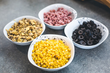 Pizza ingredients, corn, olive and salami in coup. 