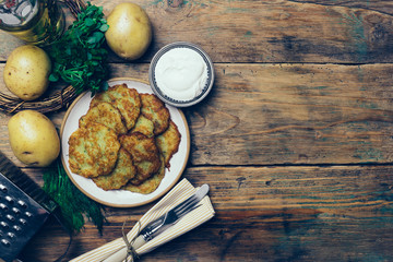 Pan-fried potato pancakes (rosti, kartoffelpuffer, latkes, draniki, hash browns): traditional potato fritters on a wooden background with sourcream and greens