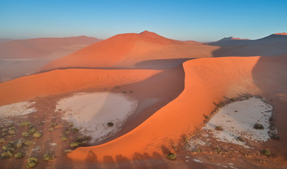 Panoramic, aerial, artistic photo of Namib dunes.  Early morning Namib desert covered in mist. Orange dunes of Namib from above. Desert landscape. Sunrise in Namib-Naukluft  desert. Traveling Namibia.