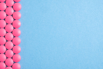 Lines of pink pills on both side on blue background. Copy space.