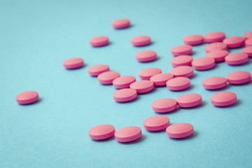 Scattered pink pills on blue background. Close up. Toned.