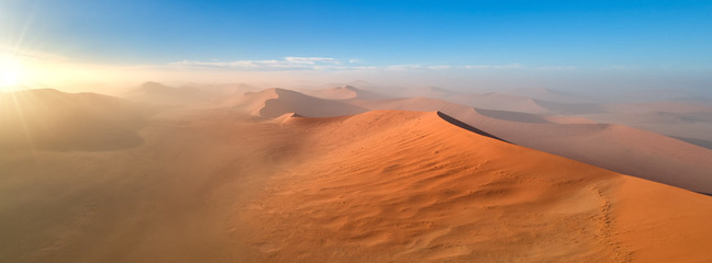 Panoramic, aerial, artistic photo of Namib dunes. Early morning Namib desert covered in mist. Orange dunes of Namib from above. Desert landscape. Sunrise in Namib-Naukluft desert. Traveling Namibia.