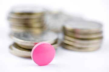 Pink pill on a stack of coins on a white background. Success in the drug business.