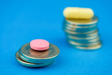 Obraz na płótnie Canvas Concept comparison and high cost of drugs. Pink pill and capsule on the stacks of coins on a blue background. Close up.