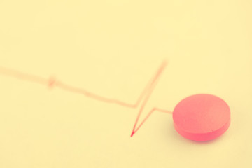 Pink tablet with the chart of red color on a white background. Concept of medicine for the heart. Toned