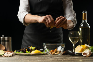 Chef pouring lemon juice with mussels with white wine salad on a dark background