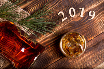 Bottle whiskey and glass with ice on a wooden table decorated cinnamons sticks, huzelnuts and christmas branch.