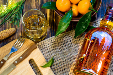 Bottle whiskey and glass with ice on a wooden table decorated cinnamons sticks, huzelnuts and christmas branch.