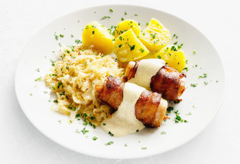 roasted bacon and rabbit belly rolls with mustard based sauce garnished with potato and cabbage sprinkled with parsley