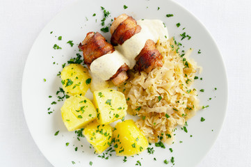 roasted rabbit belly and bacon roulades with mustard based sauce garnished with potato and cabbage sprinkled with parsley