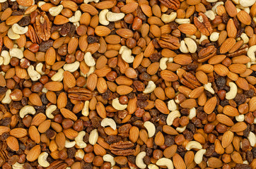 Nuts and raisins, surface and background. Snack mix of dried almonds, cashews, hazelnuts, pecans and raisins. Trail mix, student food or fodder. Raw, organic, vegan. Food photo, closeup, from above.