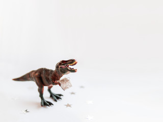 Dinosaur with present. Plastic toy with gift wrapped in silver paper. White background with star confetti. Place for text.