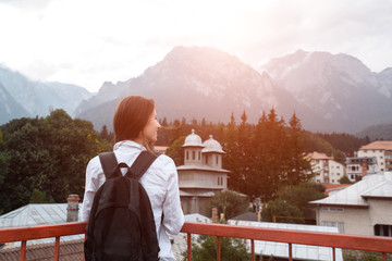 Fototapeta na wymiar Back view of smiling hipster girl with backpack on mountains background